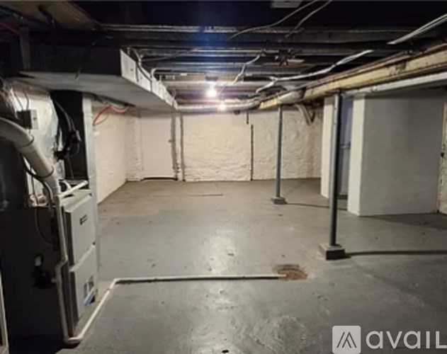 A room with a concrete floor and walls, with pipes and a light on the ceiling.