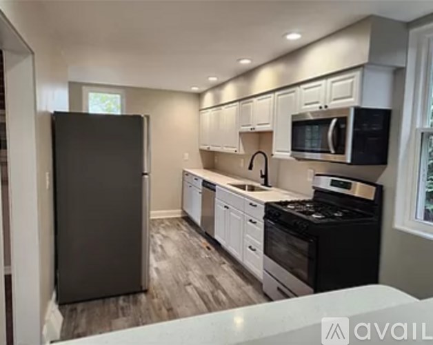 A kitchen with a black refrigerator, white cabinets, and a black stove top oven.