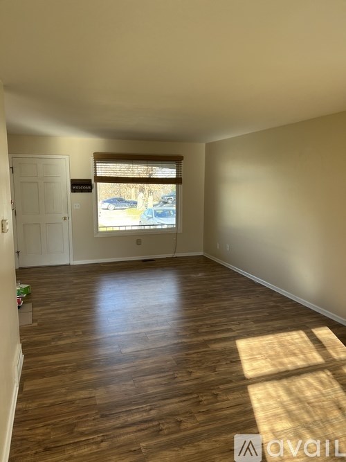 A room with wooden flooring and a window showing a parking lot outside.
