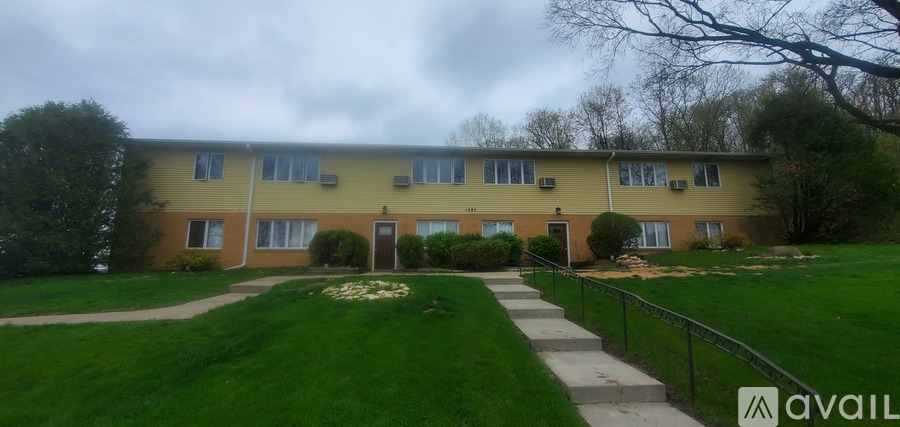 A building with a yellow and beige exterior is surrounded by a green lawn and a black fence.