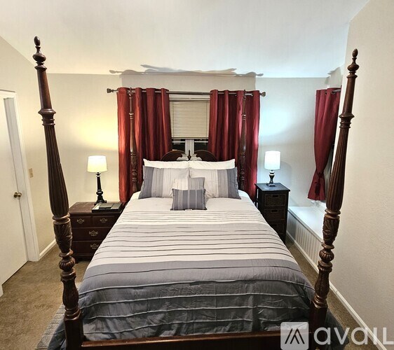 A bedroom with a four poster bed and red curtains.