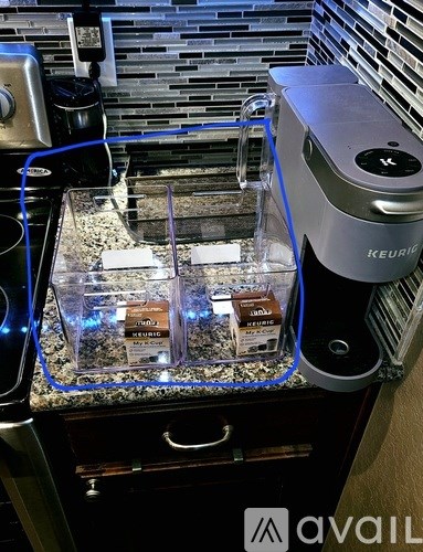 A Keurig coffee maker is on a counter with a glass container of coffee pods in front of it.