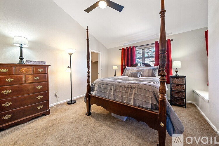 A bedroom with a four poster bed, a dresser, and a window with red curtains.