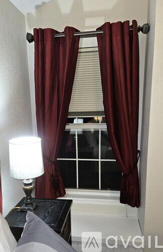 A lamp sits on a table next to a window with red curtains.