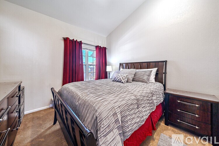A bedroom with a bed, nightstand, and window with red curtains.