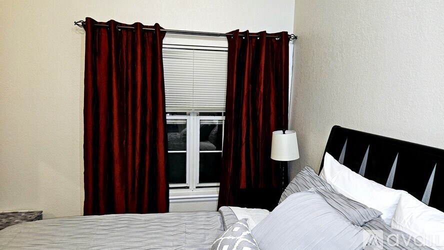 A bed with a red curtain beside a window.
