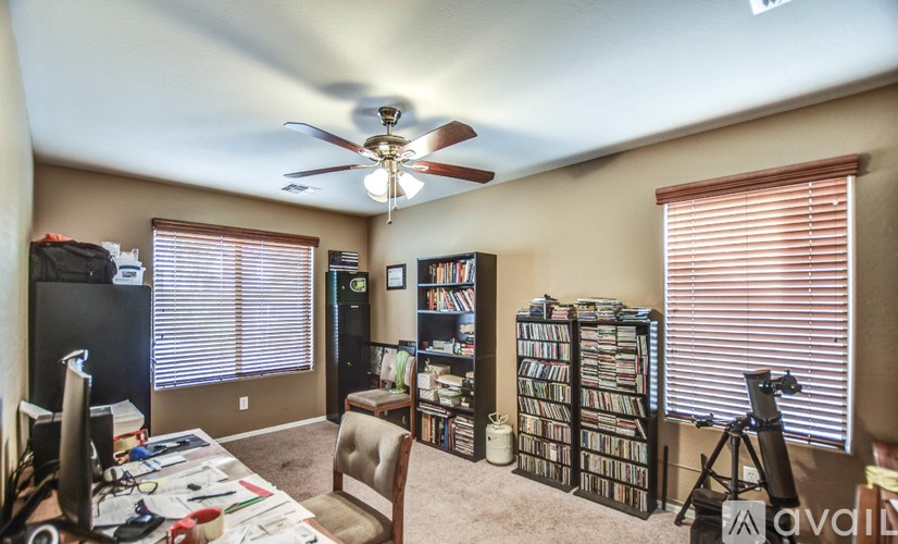 A room with a ceiling fan, a desk with a computer, and a bookshelf filled with DVDs.
