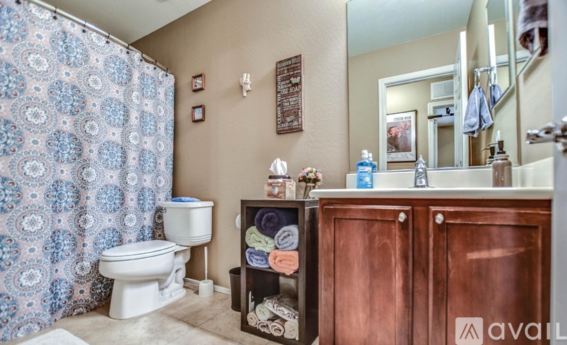 A bathroom with a toilet, a shower curtain, a towel rack, and a wooden cabinet.