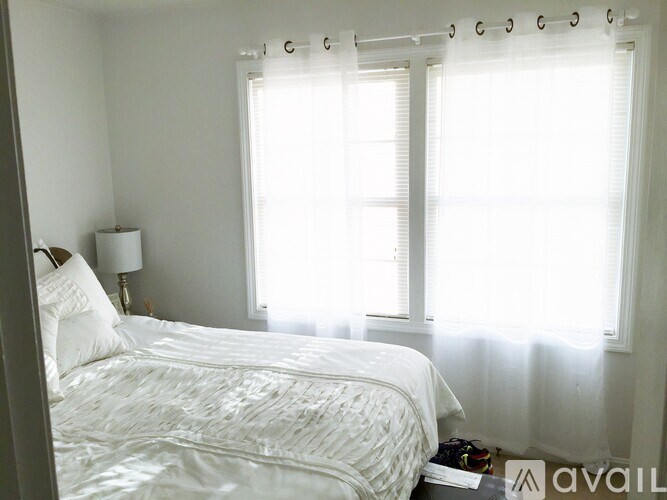 A white bedroom with a large bed and a window with curtains.