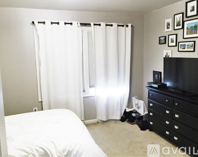 A bedroom with a bed, dresser, and a window with white curtains.