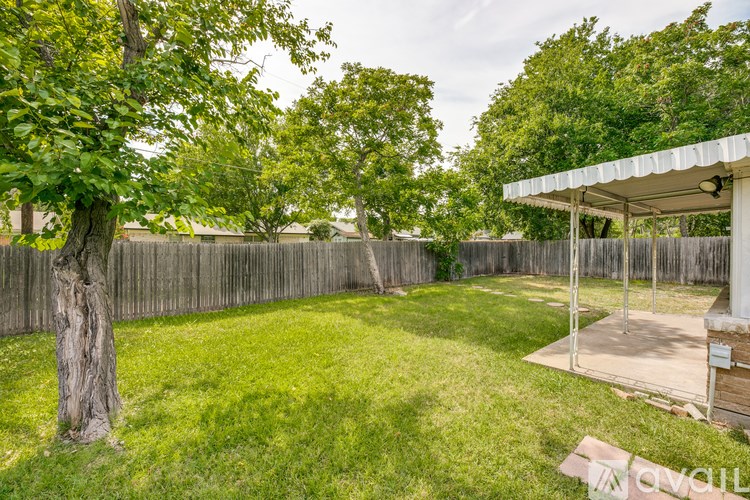 A backyard with a tree, fence, and a covered patio area.