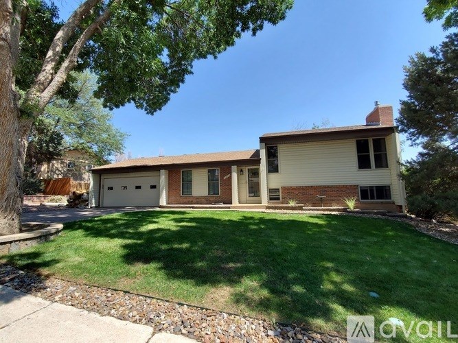 A house with a brown roof and a white garage door is surrounded by a green lawn.