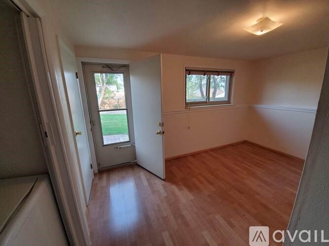 A room with wooden flooring and a window with a view of a green lawn.