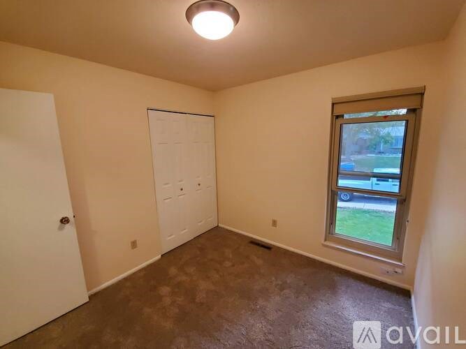 A room with a white door, a window, and a brown floor.