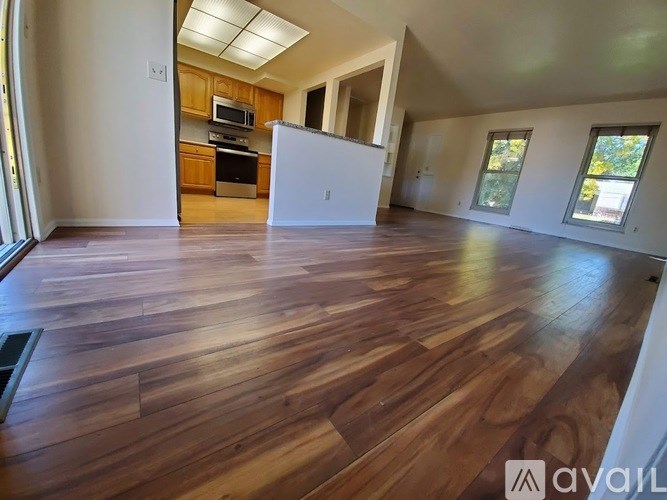 A spacious room with wooden flooring and a kitchen area in the background.