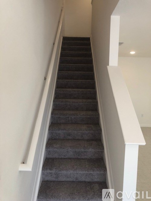A staircase with a grey carpeted runner and white balusters.