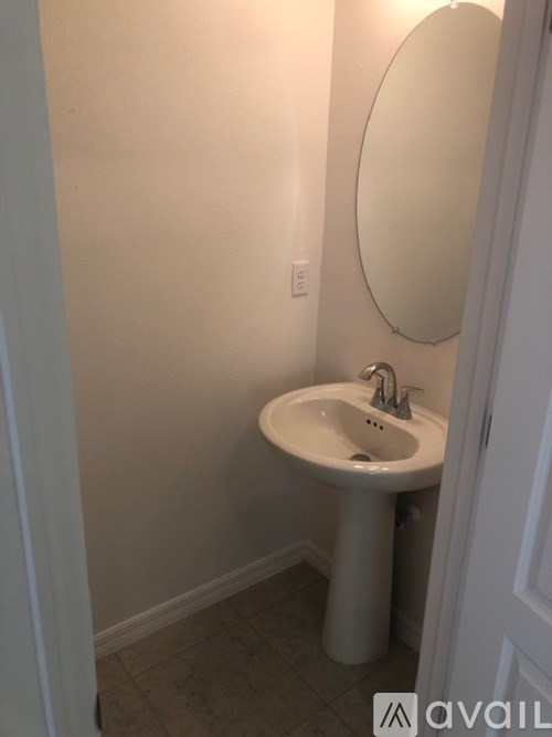 A white pedestal sink with a round mirror above it.