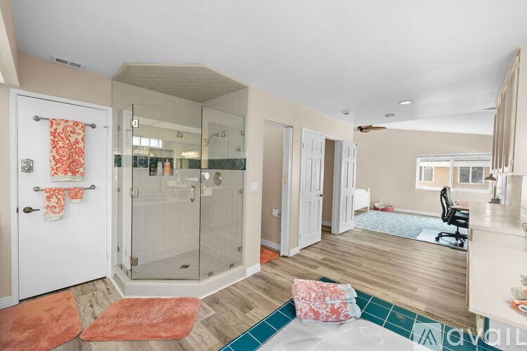 A bathroom with a glass shower door and a white door with a towel hanging on it.