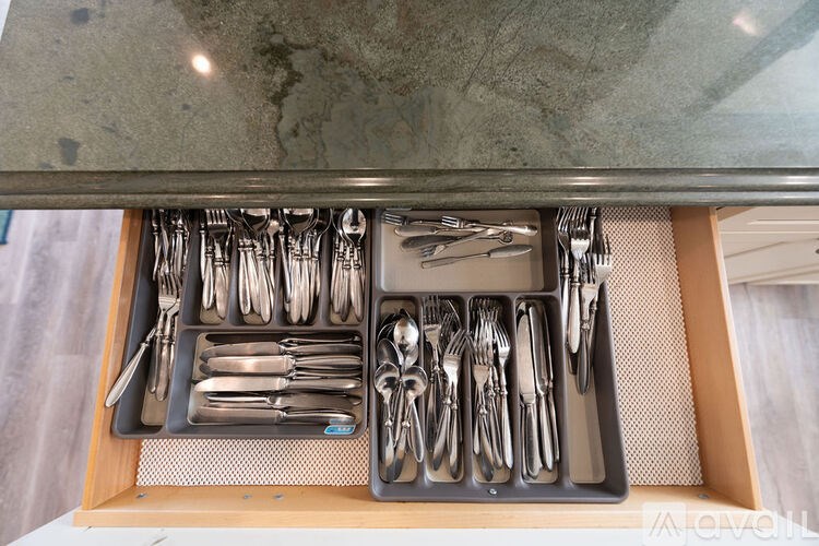 A drawer full of silverware is open under a marble countertop.