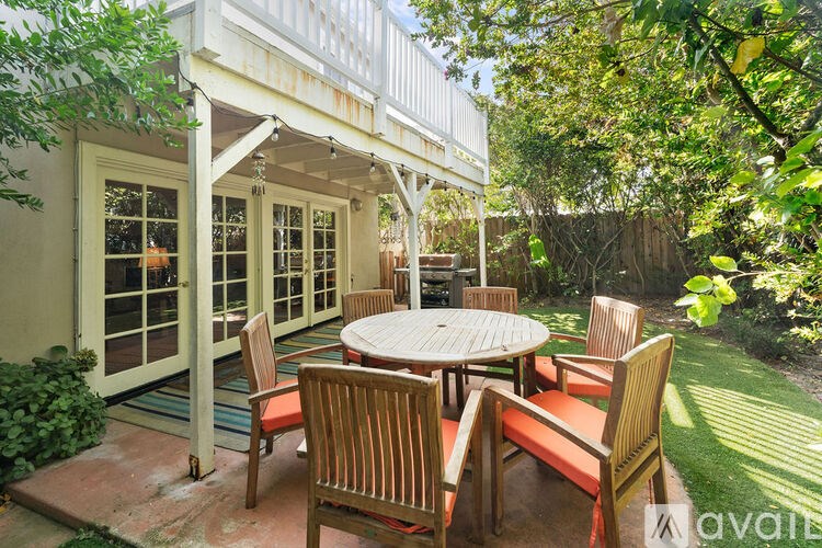 A patio with a table and chairs is surrounded by greenery.
