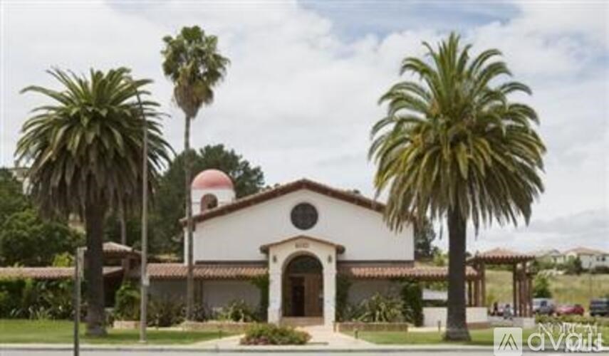 A white building with a red roof and palm trees in front.