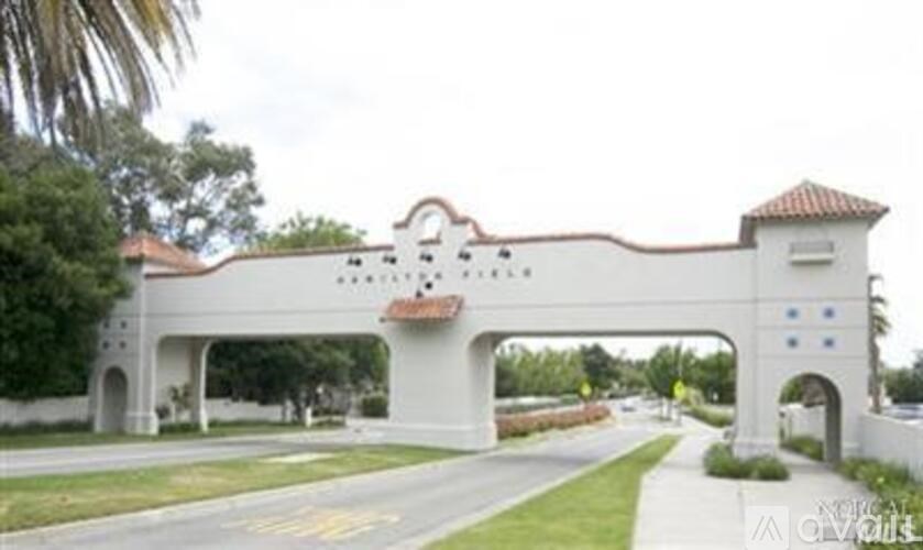 A white archway with a red tile roof and a bicycle symbol painted on the road.