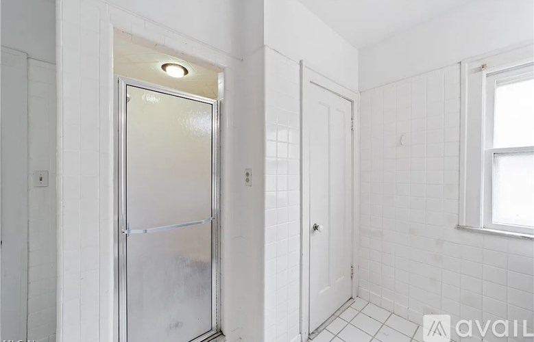 A white bathroom with a glass shower door and a window.