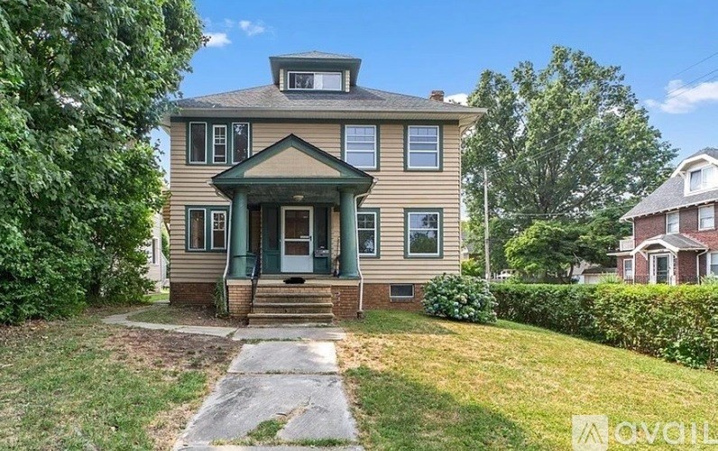 A two-story house with a green front door and a stone pathway leading to the entrance.