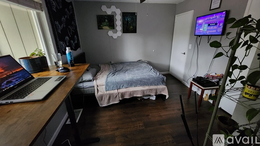 A laptop is open on a wooden desk in a room with a bed and a TV.