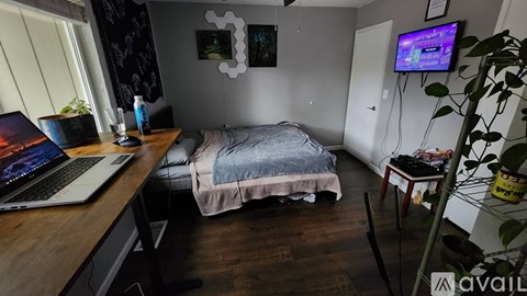 A laptop is open on a wooden desk in a room with a bed and a TV.