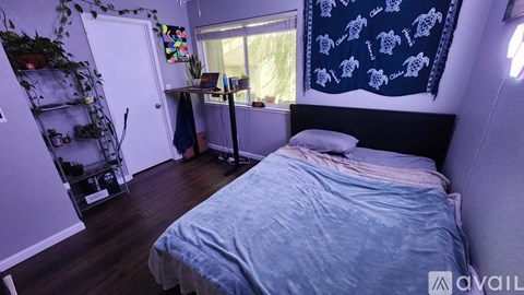 A bedroom with a bed, desk, and a window with a curtain.