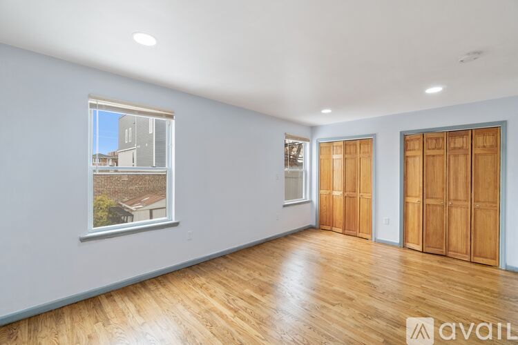 A room with wooden floors and white walls, with a window showing a view of a building outside.