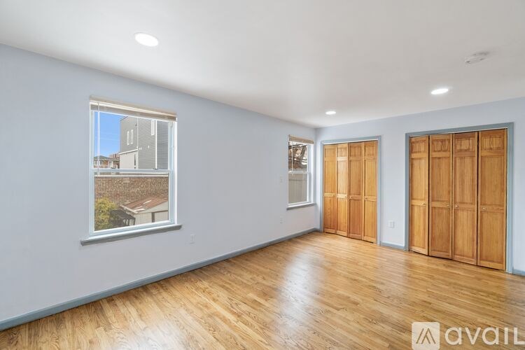 A room with wooden floors and white walls, with a window showing a view of a building outside.