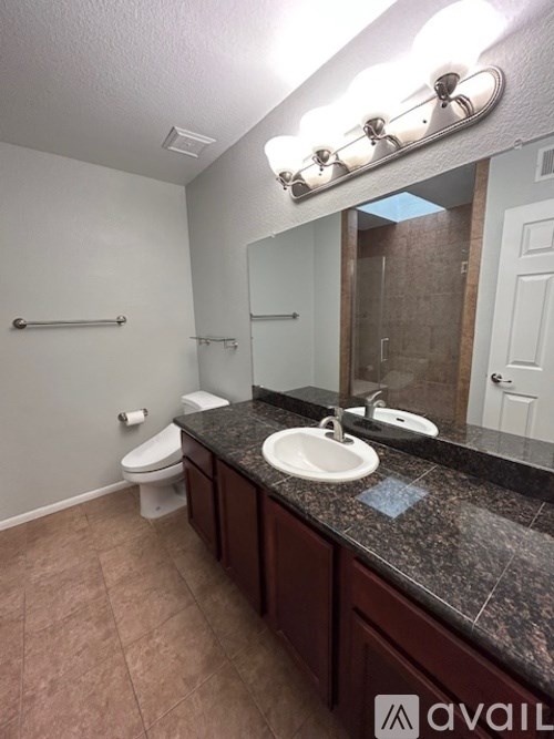 A bathroom with a sink, mirror, toilet and a towel bar.