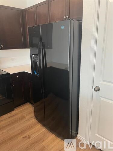 A black refrigerator in a kitchen with wooden cabinets.