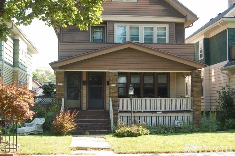 A brown house with a white porch and a tree in front.