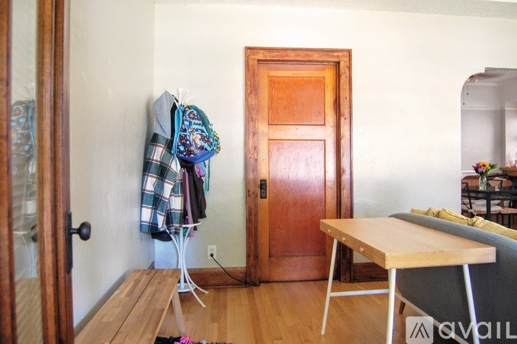 A room with a wooden door, a table, and a coat rack with clothes hanging on it.