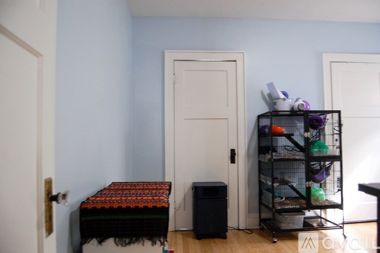 A room with a white door, a black table with a red and black blanket on it, and a black shelf with various items on it.