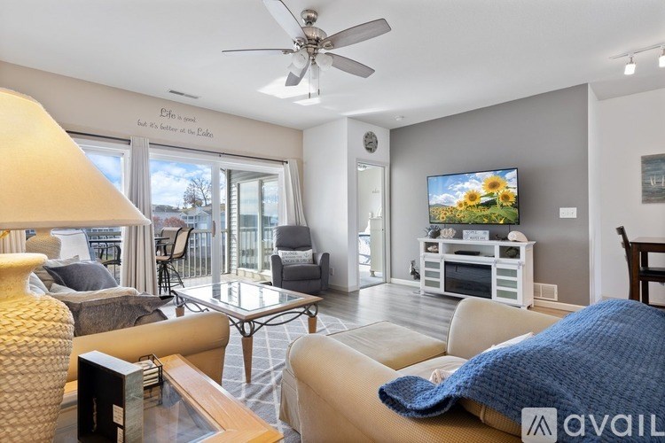 A living room with a television, a couch, a chair, a table, a lamp, and a ceiling fan.