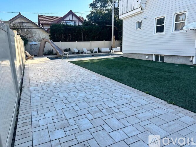 A backyard with a paved walkway and a white house.