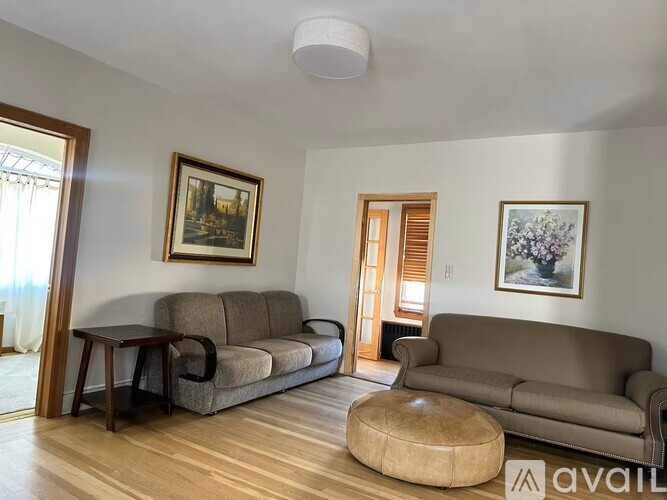 A living room with a grey couch, a brown ottoman, and two framed pictures on the wall.