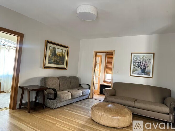 A living room with a grey couch, a brown ottoman, and two framed pictures on the wall.