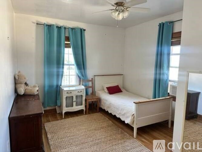 A bedroom with a bed, a dresser, a nightstand, and a window with blue curtains.
