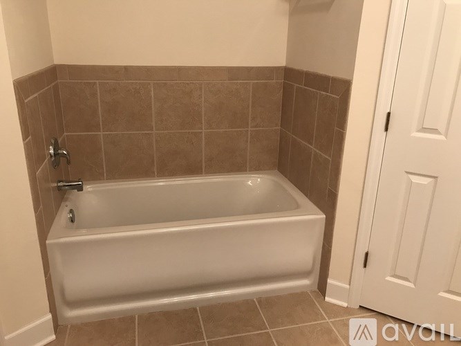 A white bathtub in a bathroom with brown tiles.