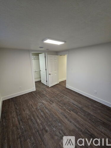 A room with wood flooring and a white wall with a doorway leading to another room.