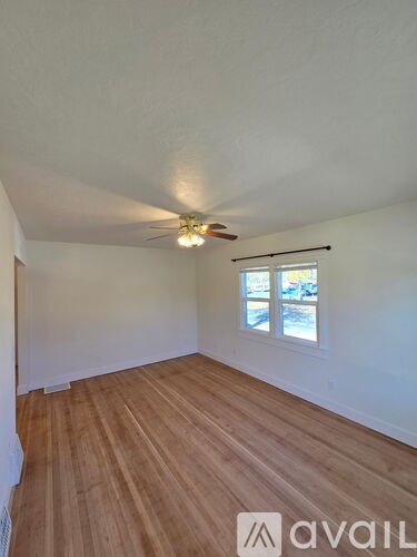 A room with wooden floors and white walls, with a window and a chandelier.