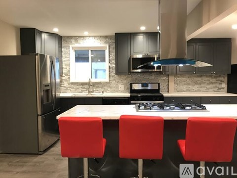 A modern kitchen with a white island and red chairs.
