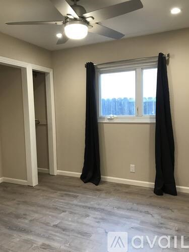 A room with a ceiling fan and a window with curtains.