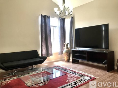 A living room with a black sofa, a glass coffee table, a television, and a chandelier.
