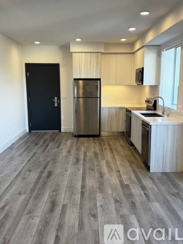 A kitchen with a black door, stainless steel refrigerator, and wooden flooring.